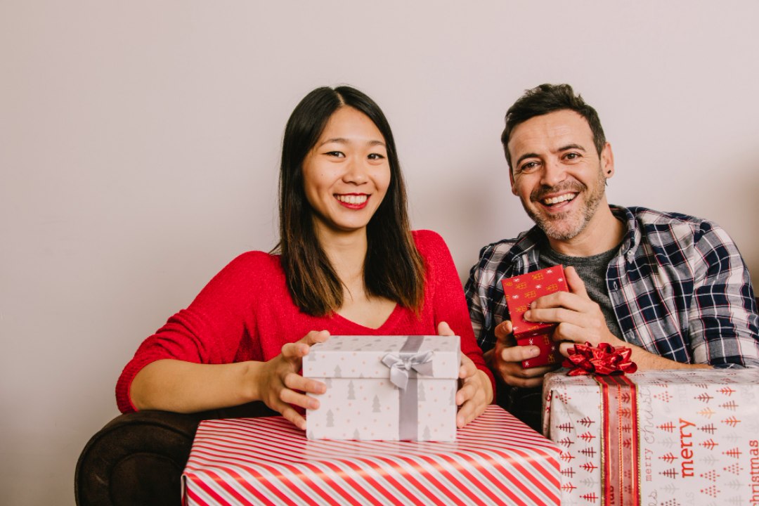 Pasangan gembira memegang pelbagai kotak hadiah berwarna, melambangkan pilihan pembungkusan dari pembekal kotak hadiah Malaysia
